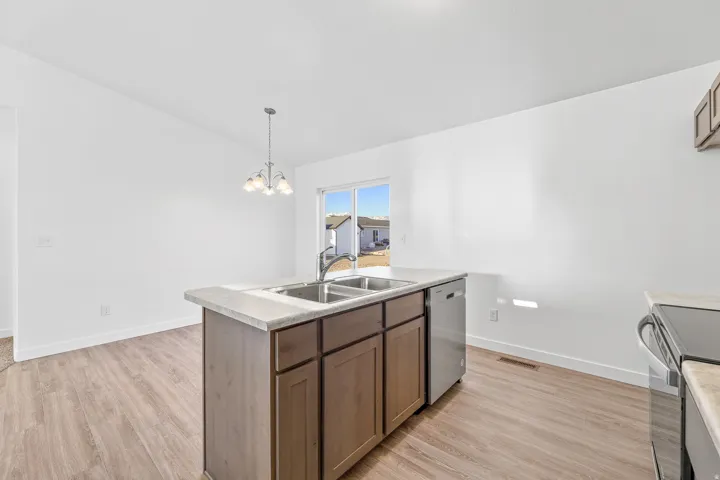 Kitchen island with integrated stainless steel sink and dishwasher, wood-finish flooring, and a contemporary chandelier