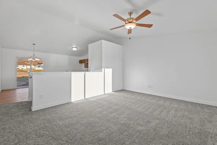 Expansive room featuring light gray carpeting, neutral wall finishes, and a ceiling fan with integrated lighting