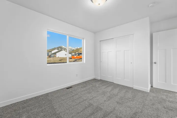 Bright corner bedroom with expansive windows framing natural light and mountain scenery, neutral wall finishes, neutral-tone carpeting, and multiple closet doors providing ample storage