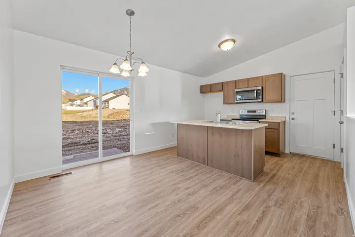 Sliding glass patio door, wood-finish flooring, kitchen island with integrated sink, stainless steel appliances, and wood cabinetry