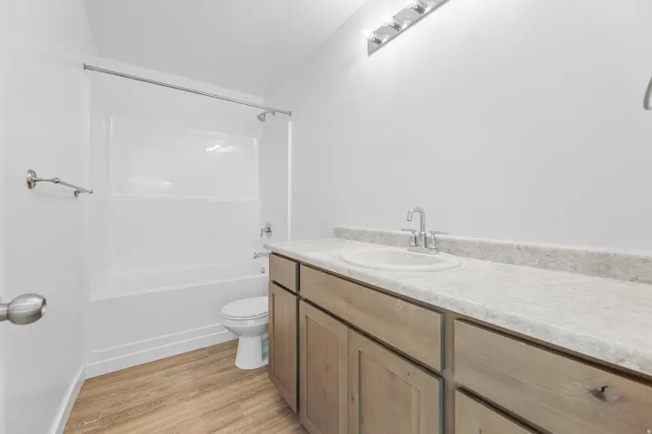 White bathroom featuring a built-in tub with shower, single vanity with wood-finish cabinetry, and wood-finish flooring