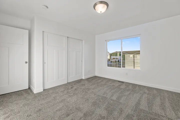 Neutral carpeting, white paneled doors, sliding closet doors, and an overhead flush-mount light fixture