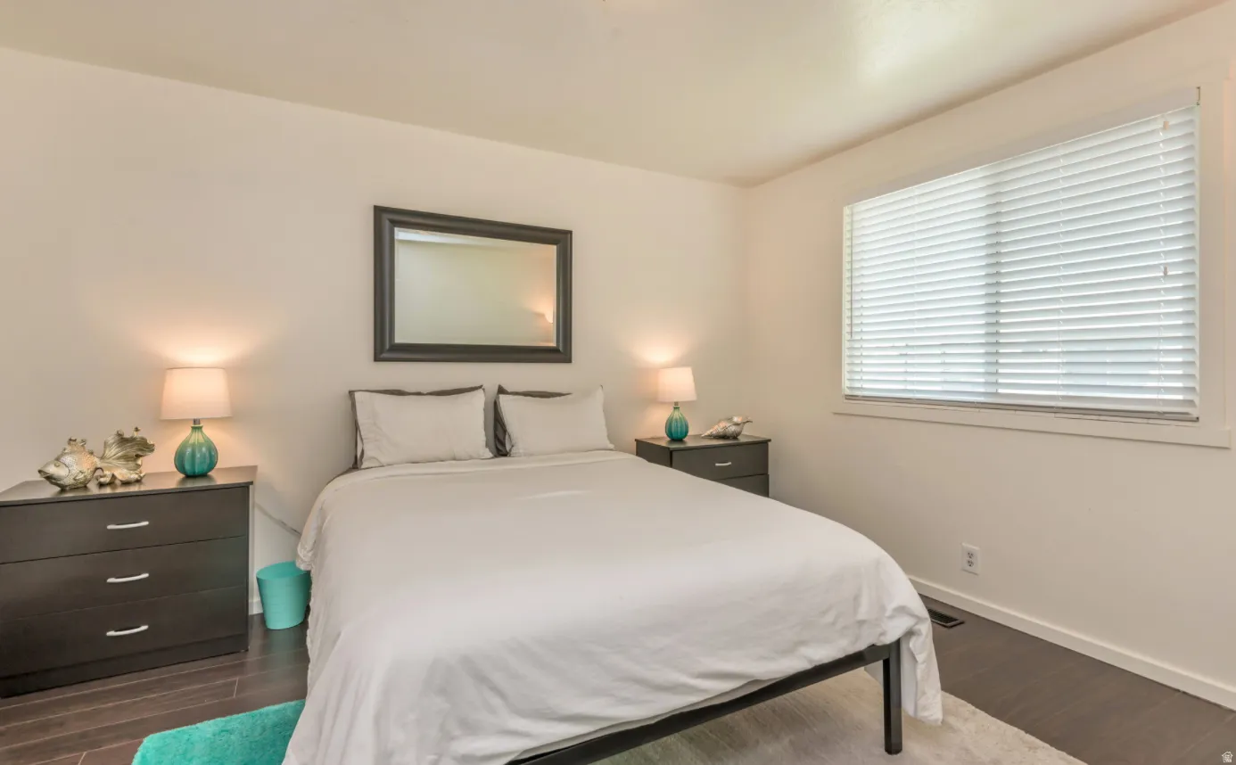 White walls, dark wood-finish flooring, and a large window with horizontal blinds
