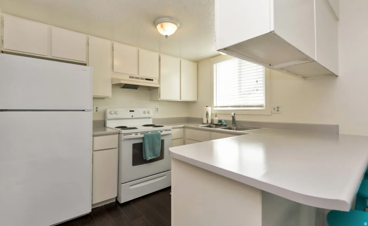 Kitchen featuring white cabinetry, white appliance package, light-toned countertops, wood-finish flooring, and an integrated breakfast bar