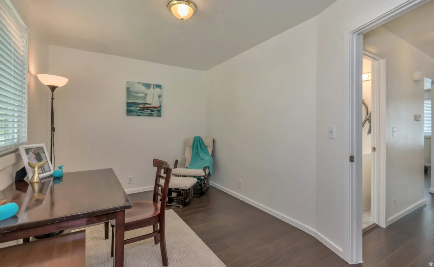 White walls, dark wood-finish flooring, and a window with horizontal blinds