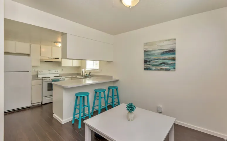Kitchen featuring white cabinetry, white appliances, light-toned countertops, and wood-finish flooring