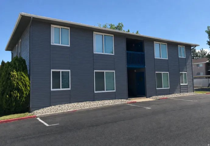 Two-story exterior with horizontal siding, multiple windows, a central balcony, and a paved parking area