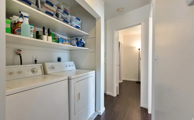 Laundry area featuring a side-by-side washer and dryer, open shelving, and wood-finish flooring