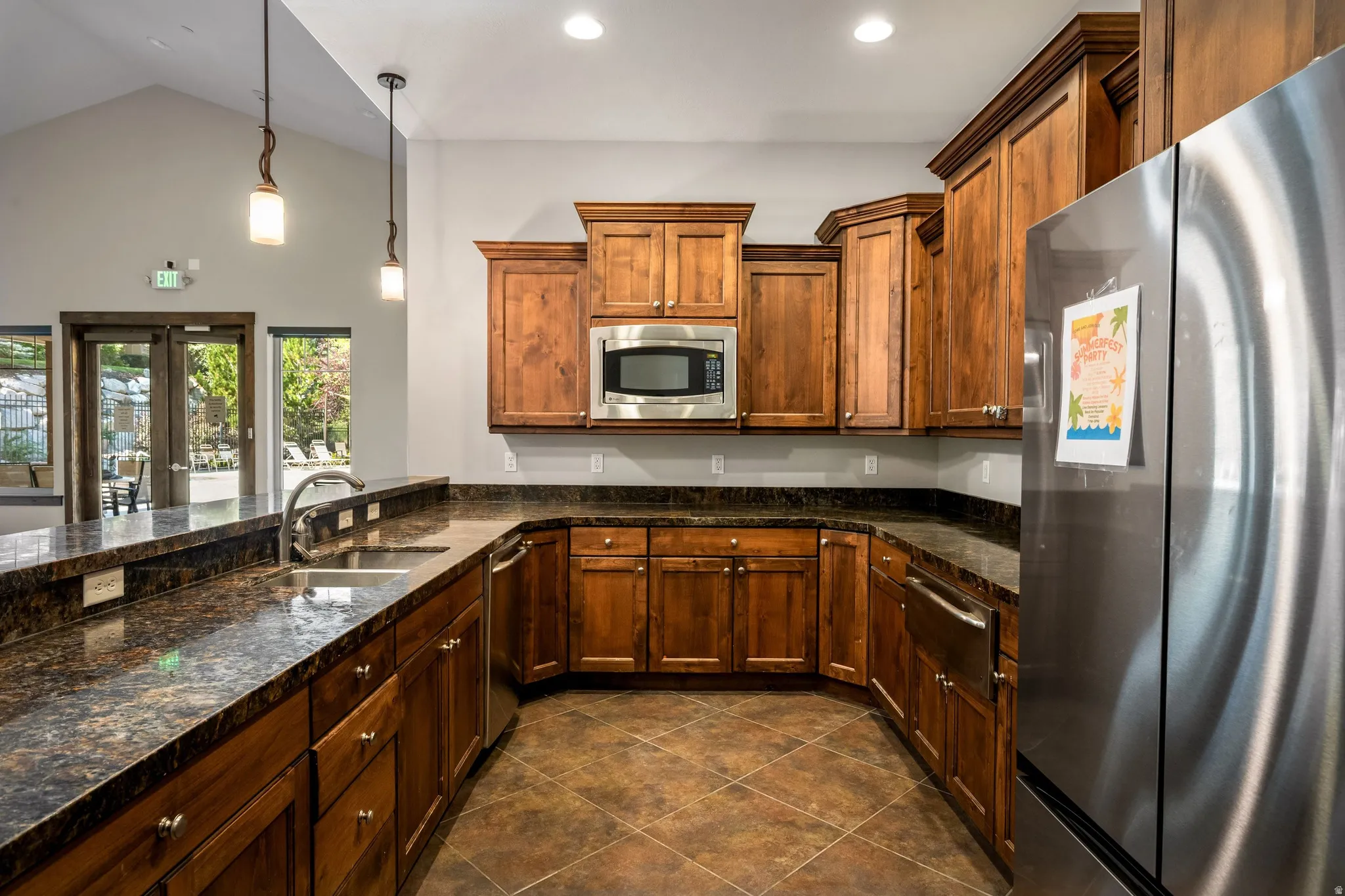 Vaulted ceiling, wood-finish cabinetry, stainless steel appliances, dark stone-finish countertops, and wood-look tile flooring