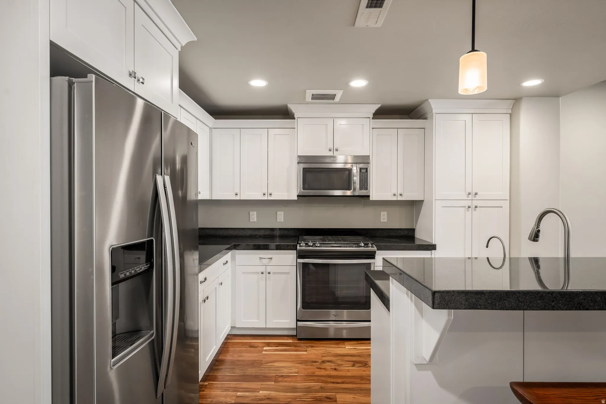 White shaker cabinetry, stainless steel appliances, dark stone countertops, wood-finish flooring, and recessed lighting