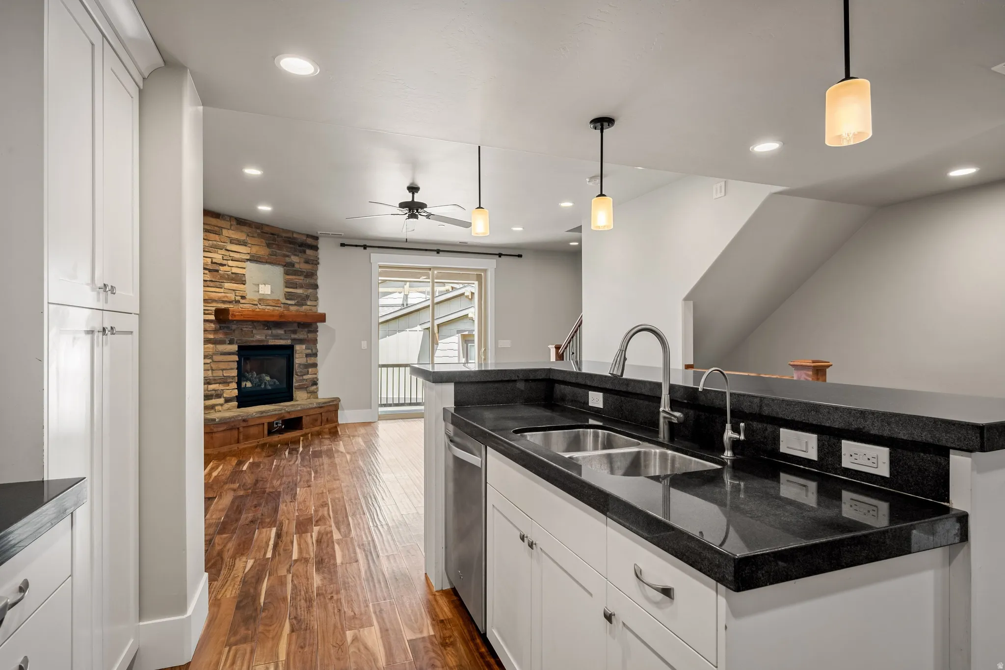 Kitchen island with double basin stainless steel sink, dark countertops, and white cabinetry
