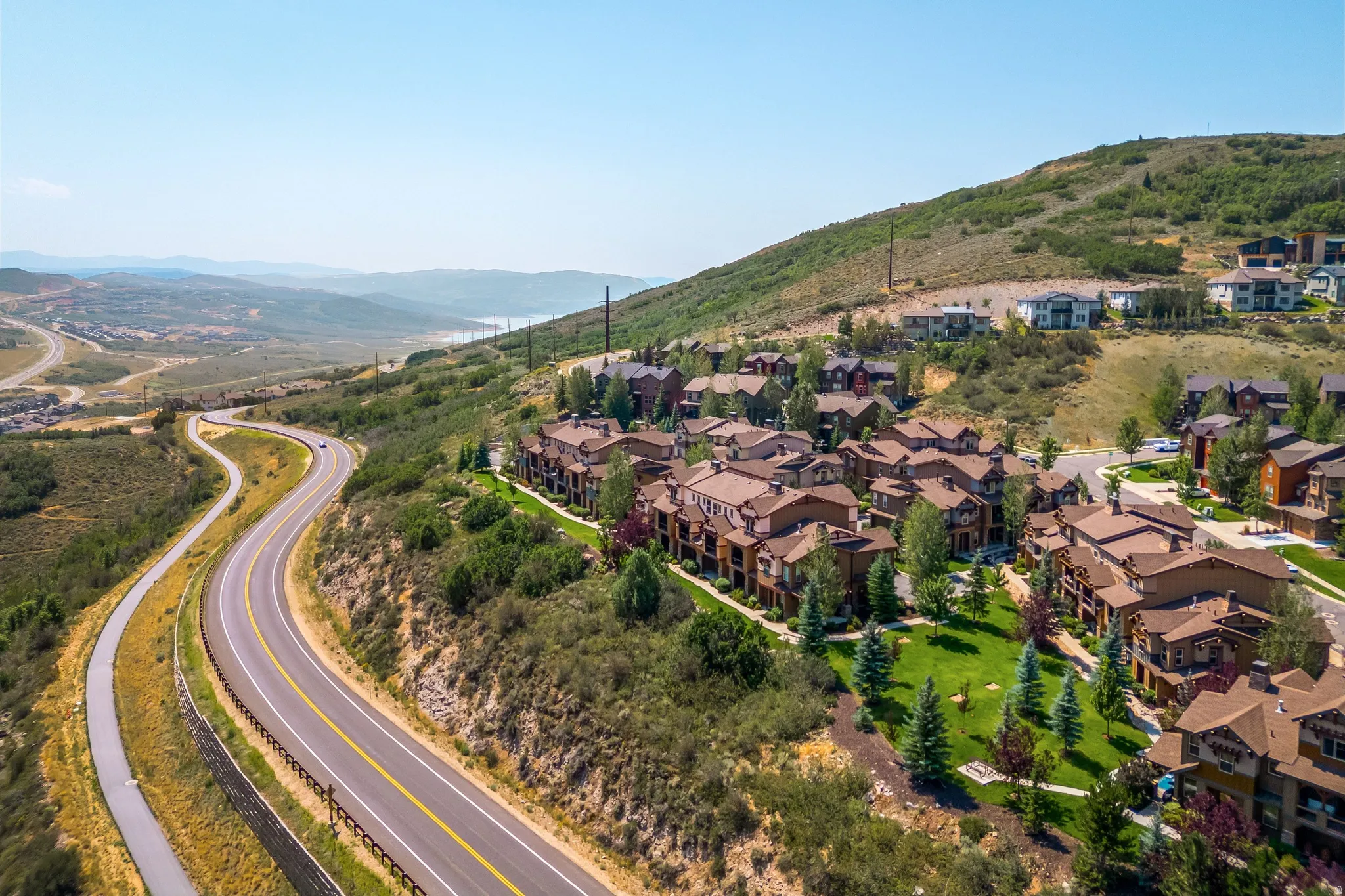 Hillside residential community featuring Mediterranean-inspired architecture with terracotta tile roofing, manicured landscaping, and mature trees throughout the development