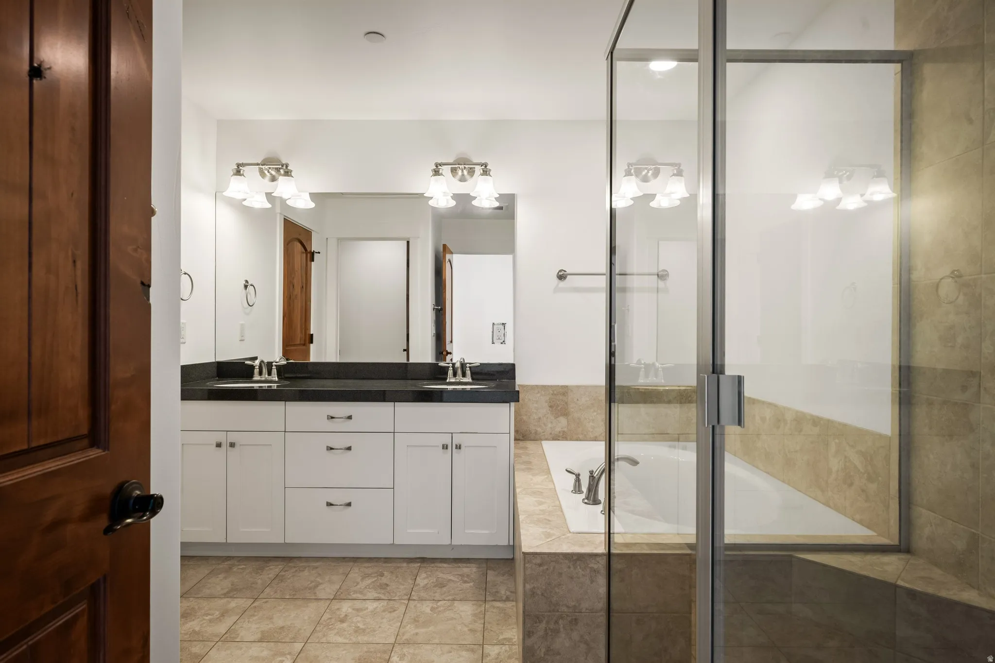 Dual vanity with dark countertops, white cabinetry, a built-in bathtub, and a separate glass-enclosed shower