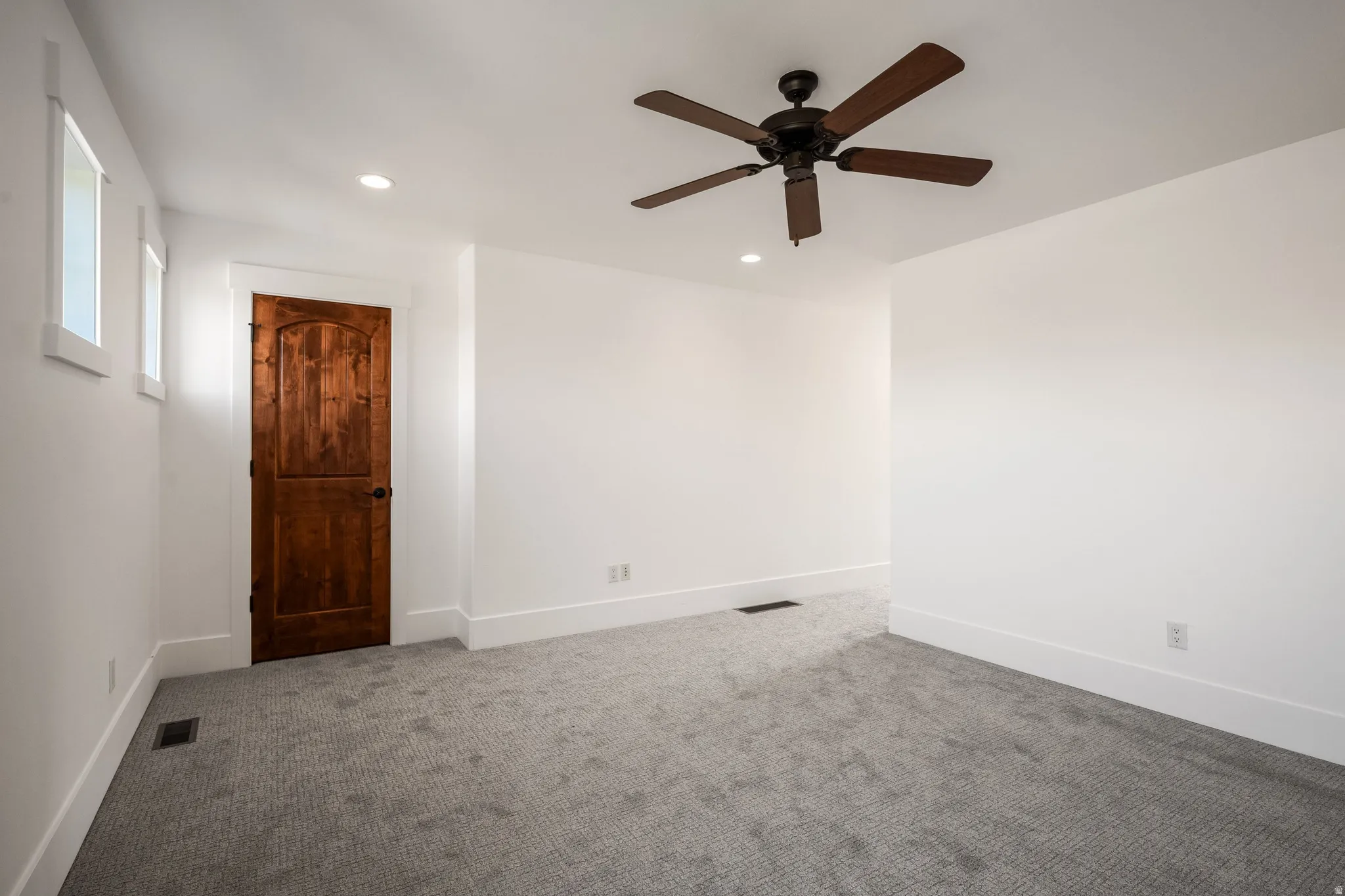 Recessed ceiling lighting, a ceiling fan with dark wood-finish blades, and a solid wood-panel door