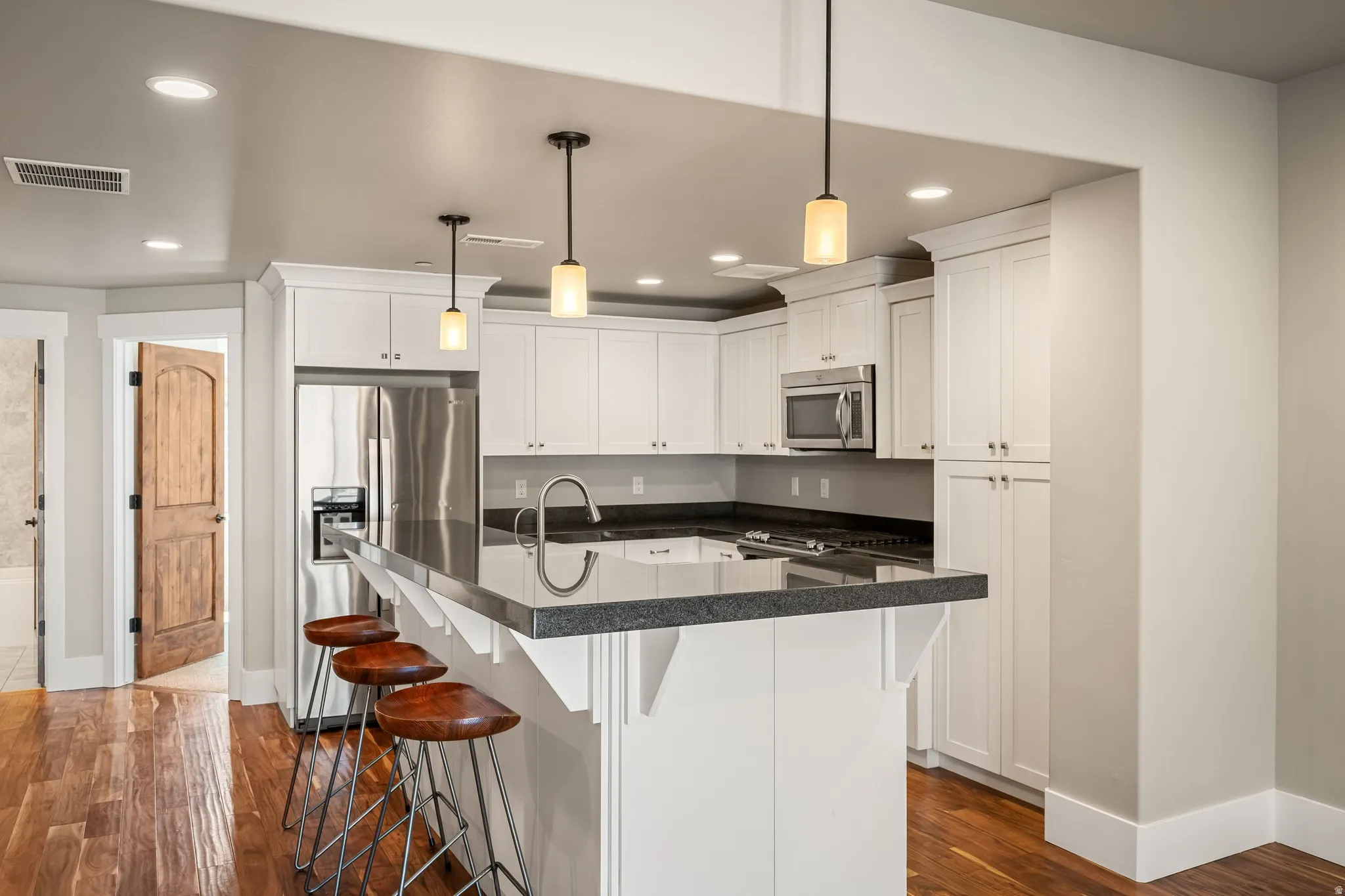 Kitchen featuring white shaker cabinetry, stainless steel appliances, dark countertops, a breakfast bar, and recessed lighting