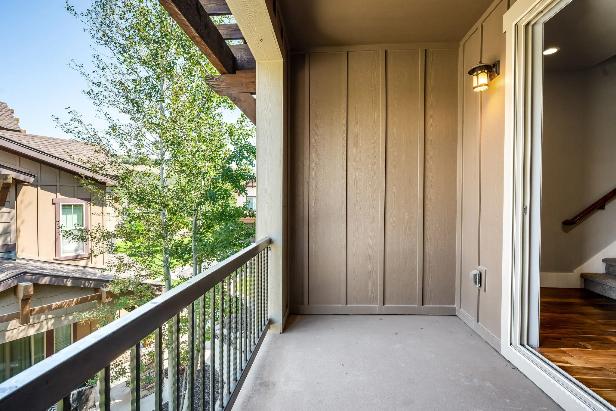 Private balcony with a metal railing, wood pergola, exterior wall sconce, and sliding glass door