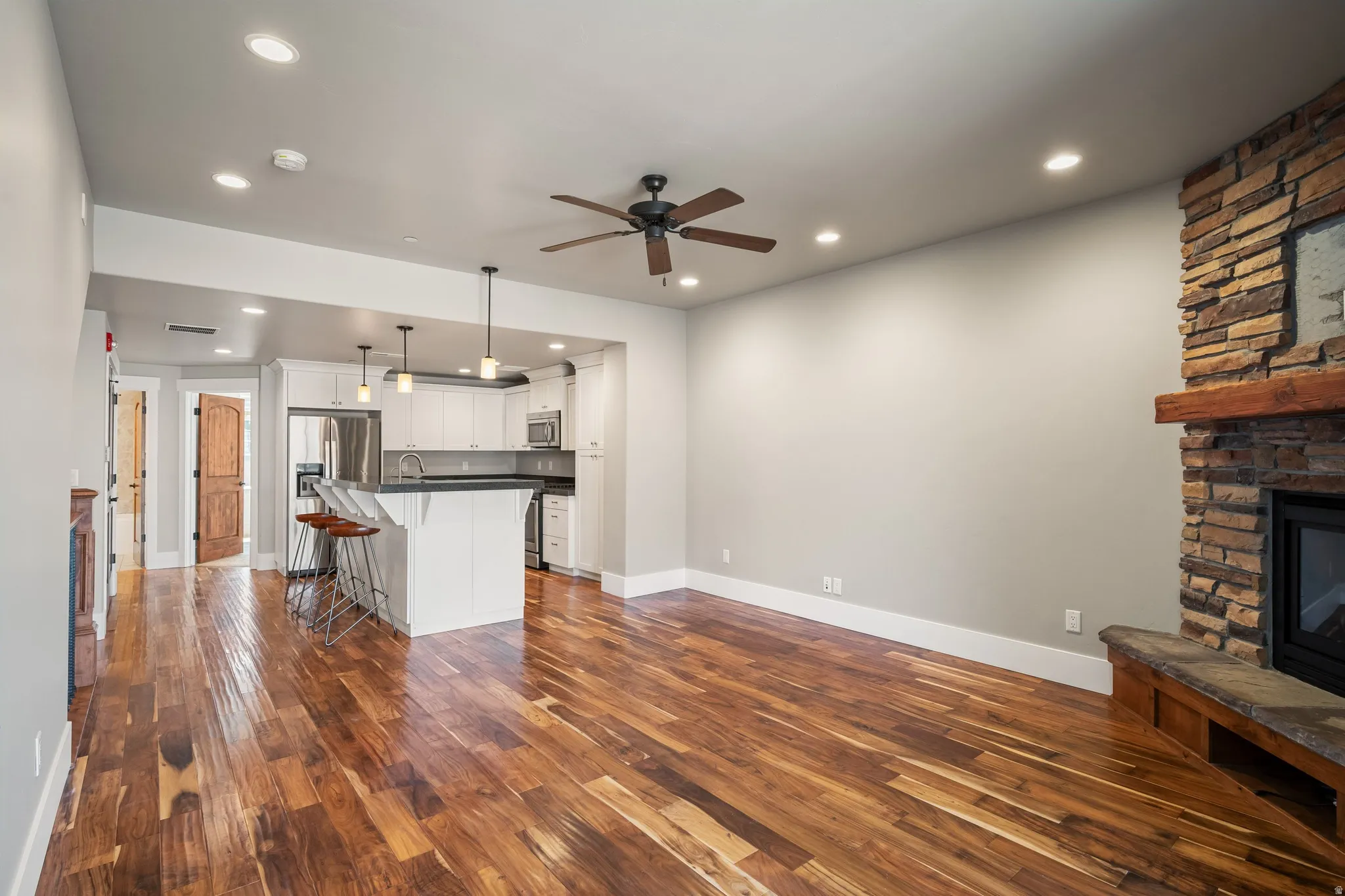 Wood-finish flooring throughout, recessed lighting, and a stone-clad fireplace with a wood mantel