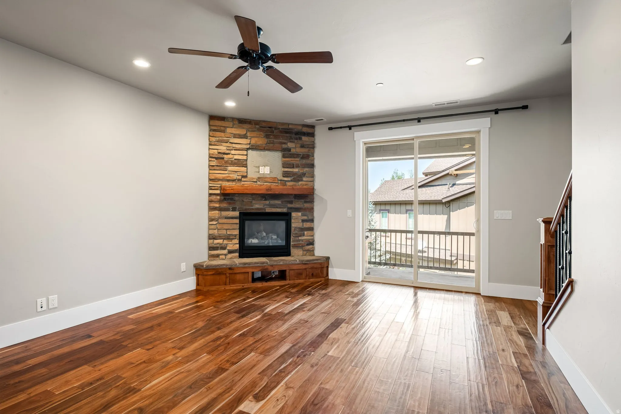Hardwood-finish flooring, recessed lighting, corner stone fireplace with wood mantel, ceiling fan, and sliding glass door with balcony access