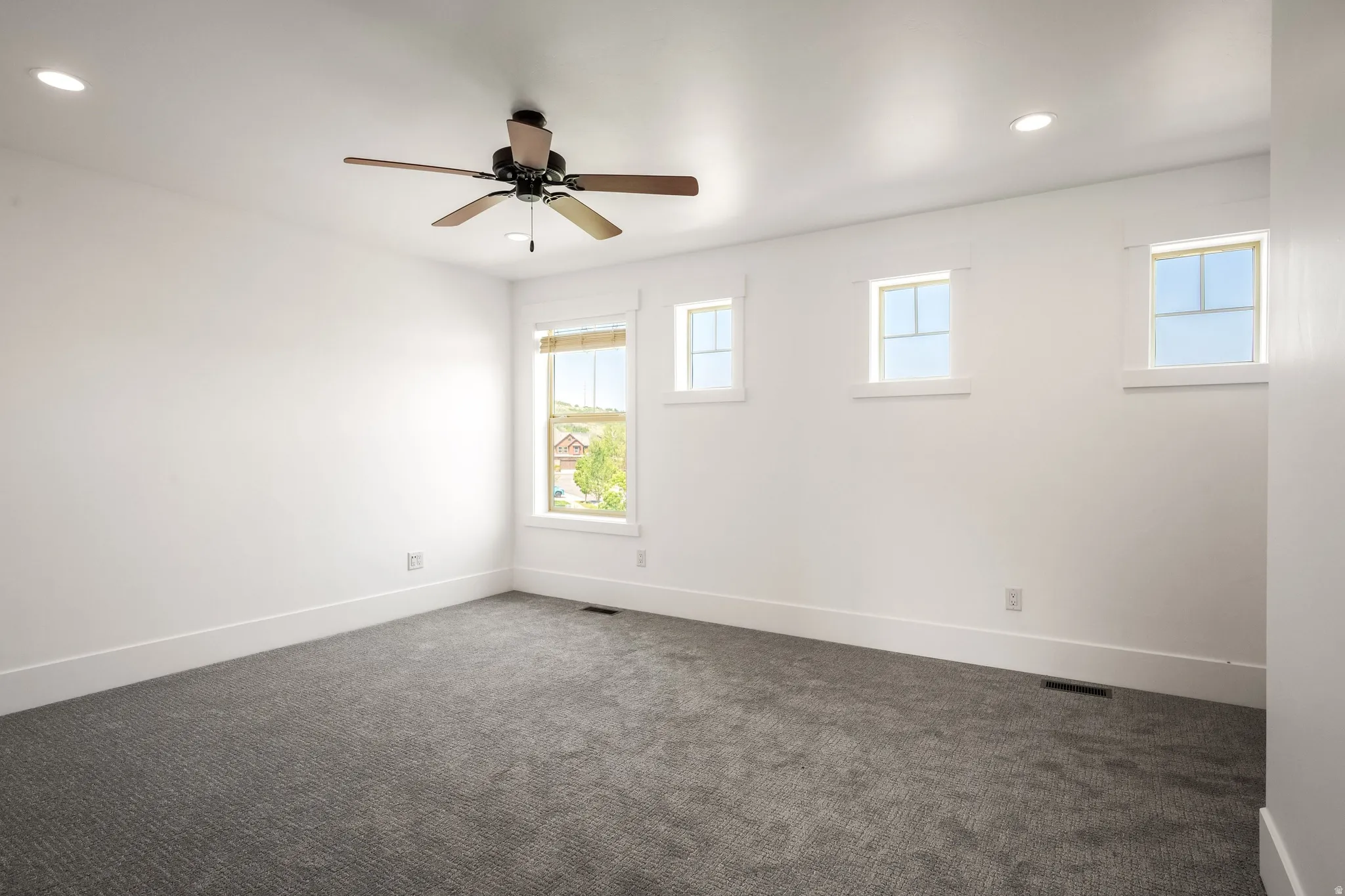 Recessed lighting, ceiling fan, white trim, multiple windows, and gray patterned carpeting