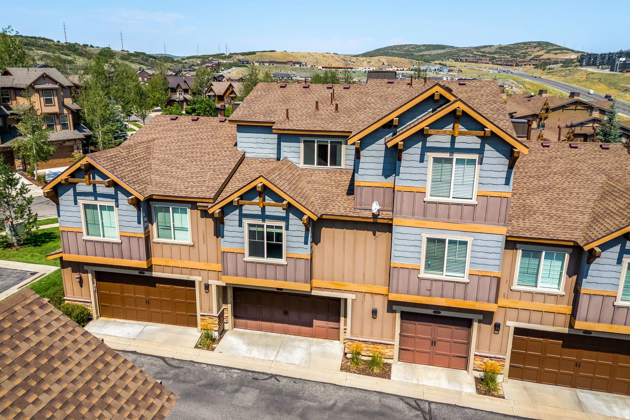 Townhome exterior featuring multiple dormer windows, brown shingle roofing, and attached garages