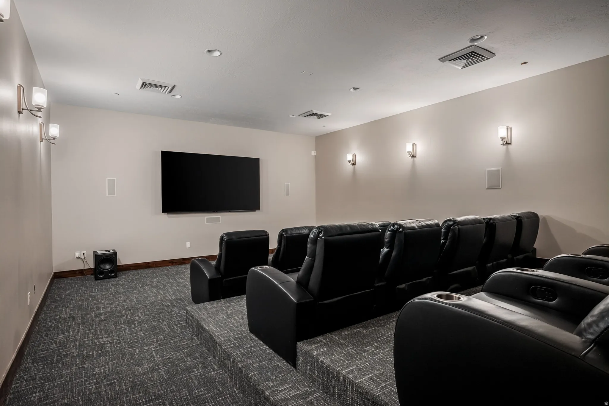 Dedicated media room featuring tiered seating, wall-mounted television, recessed ceiling lights, wall sconces, and carpeted flooring