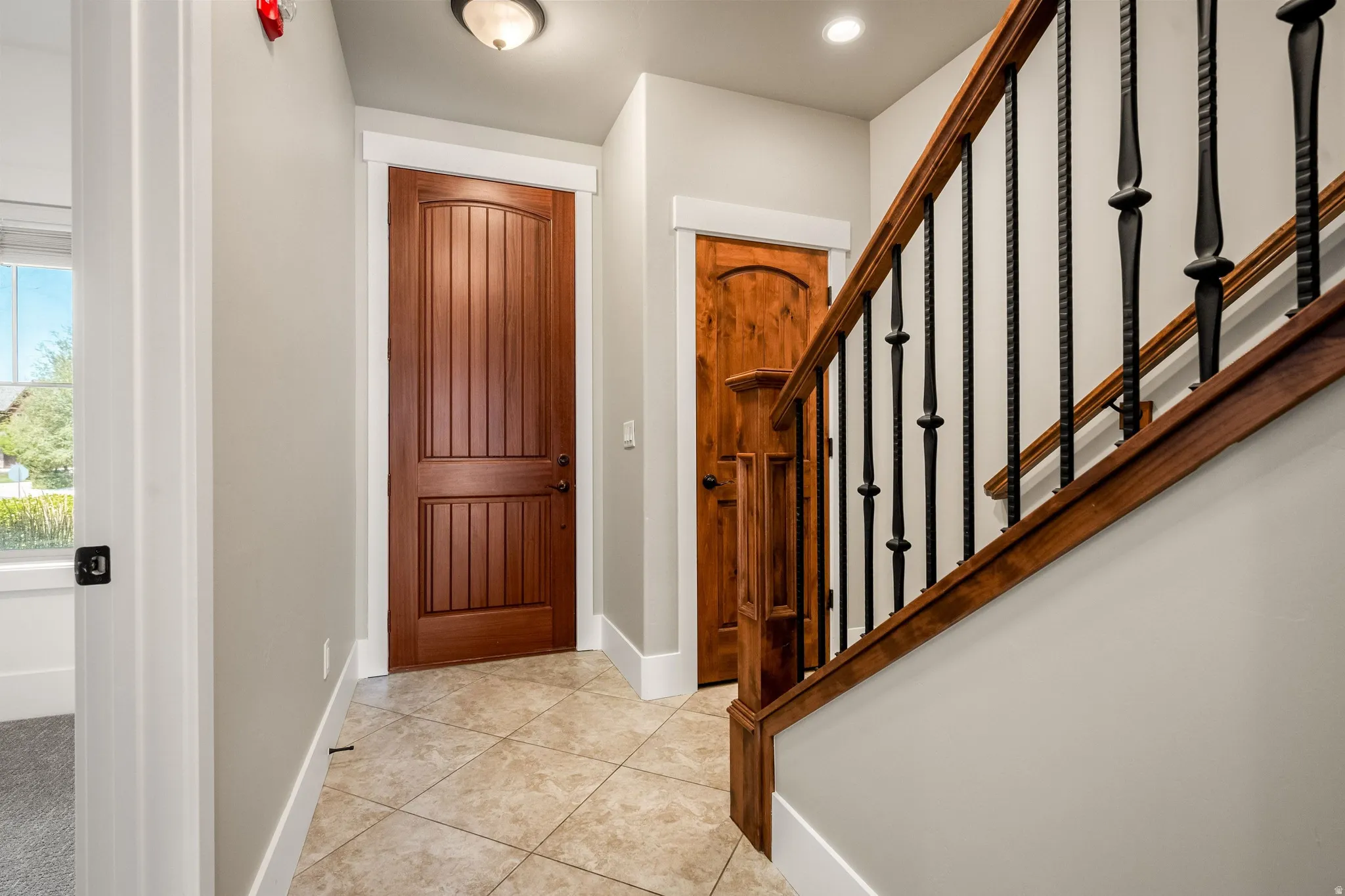 Wood-finish doors, wrought iron balusters, wood-finish handrail, neutral wall paint, and tiled flooring