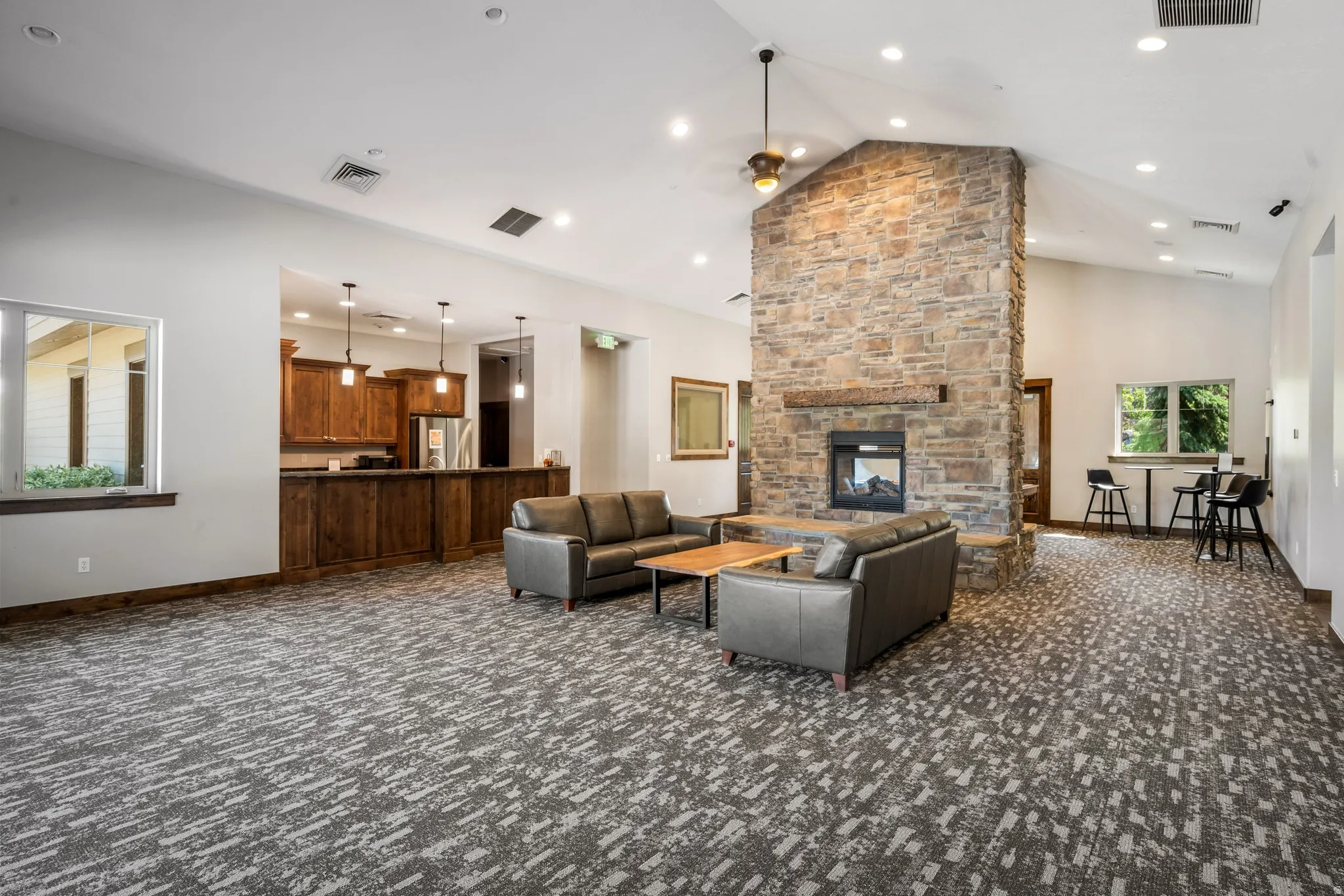 Vaulted ceiling with recessed lighting, stone-clad fireplace, wood-finish cabinetry, built-in bar, and contemporary patterned carpet
