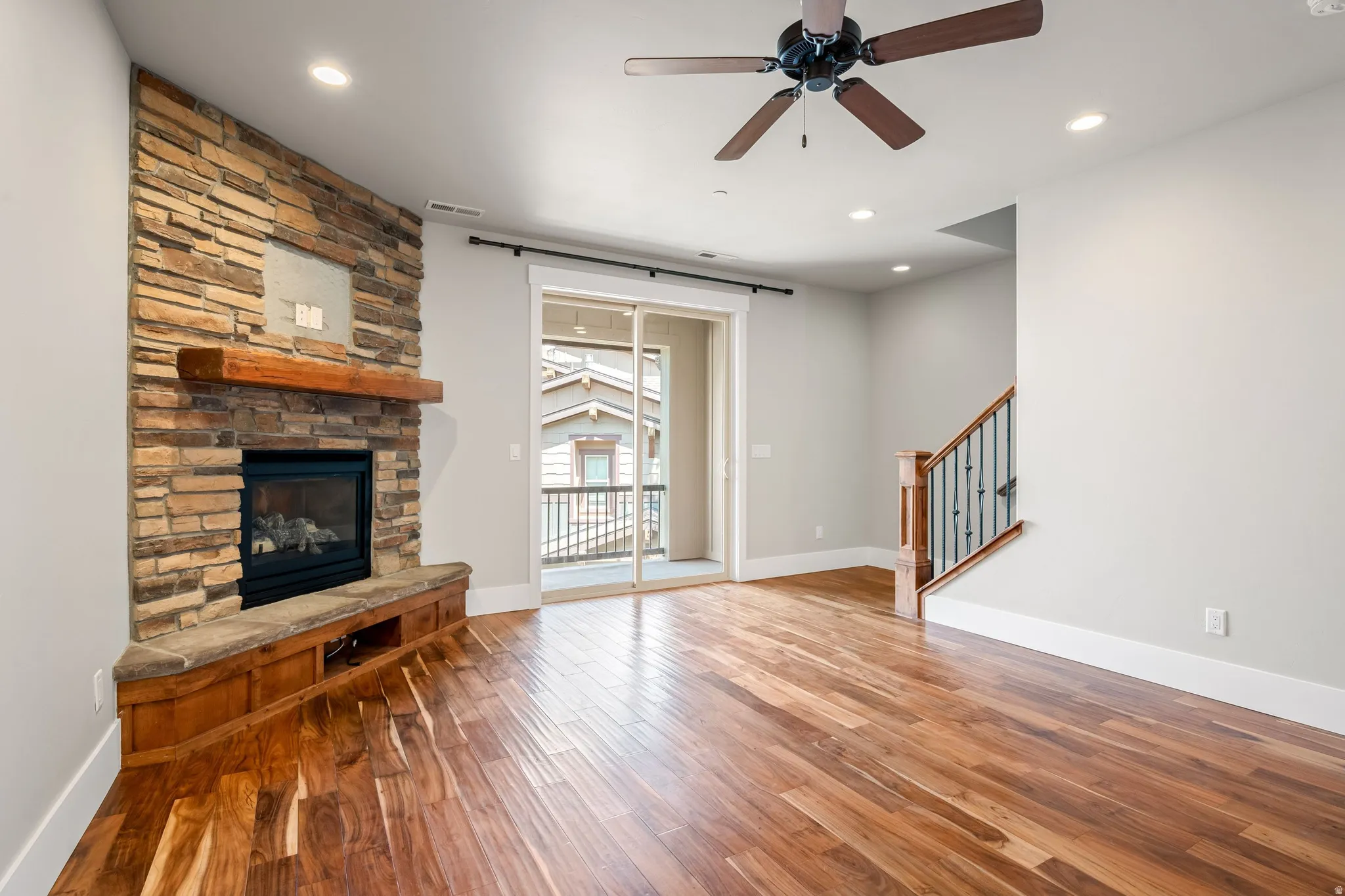 Stone-faced fireplace with wood mantel and built-in media console, wood-finish flooring, recessed lighting, and a ceiling fan