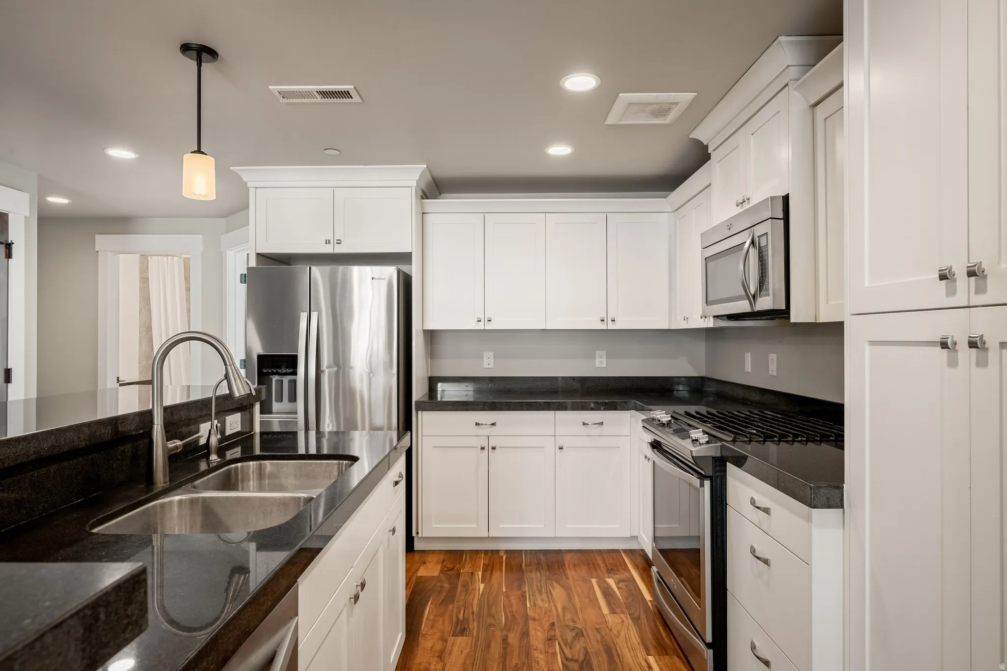 Kitchen with dark countertops, wood-finish flooring, white cabinetry, stainless steel appliances, and a double basin sink with an arched faucet