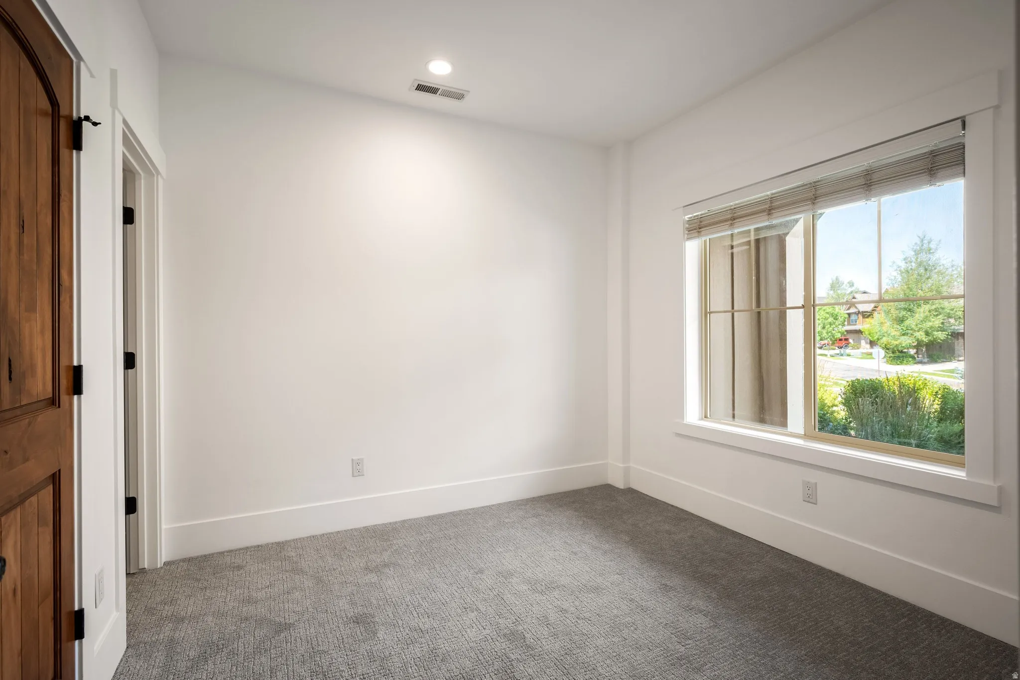 Arched wood-paneled door with dark hardware, recessed ceiling lighting, window with slatted blinds, and patterned carpeting