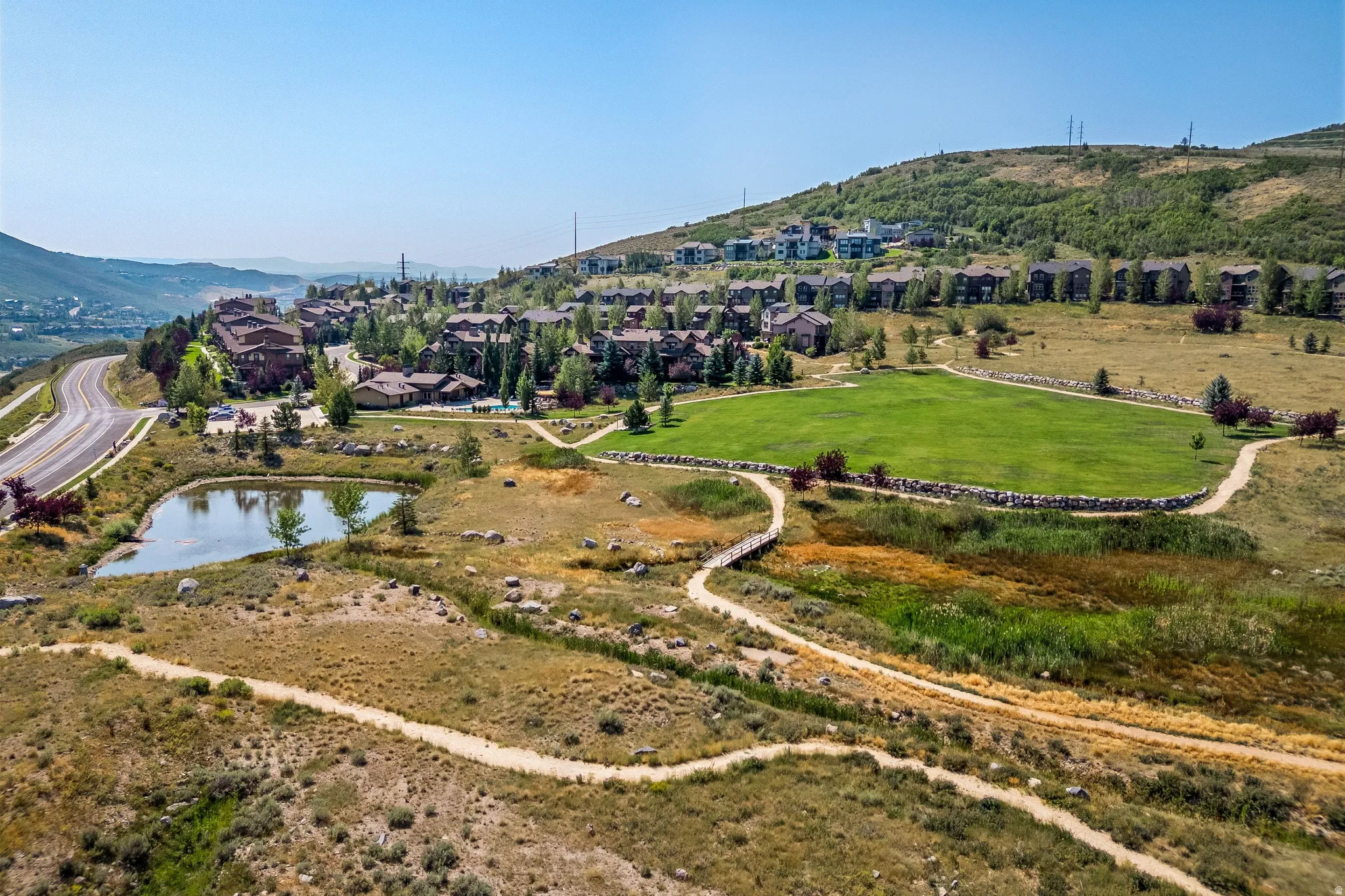 Hillside property with a large green area, surrounded by walking paths, and featuring a pond with established vegetation