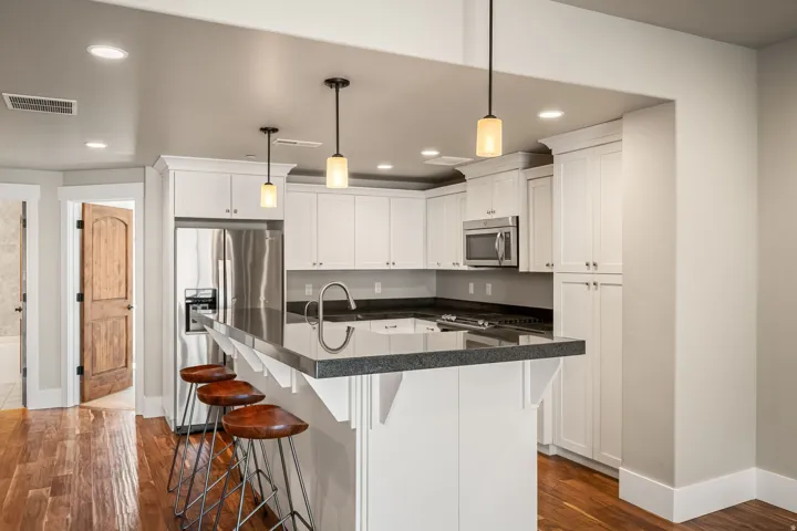 Kitchen featuring white shaker cabinetry, stainless steel appliances, dark countertops, a breakfast bar, and recessed lighting