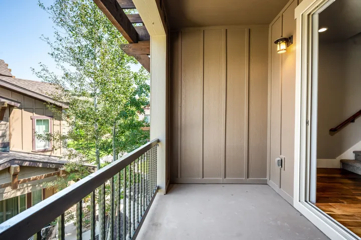 Private balcony with a metal railing, wood pergola, exterior wall sconce, and sliding glass door