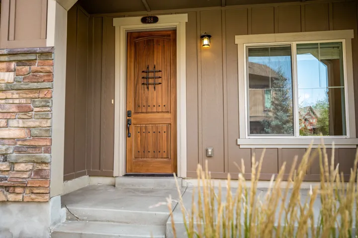 Crafted wood-paneled door with decorative ironwork, stone veneer column, concrete porch, and exterior lighting fixture