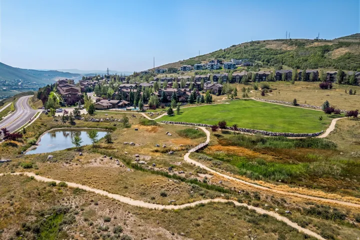 Hillside property with a large green area, surrounded by walking paths, and featuring a pond with established vegetation