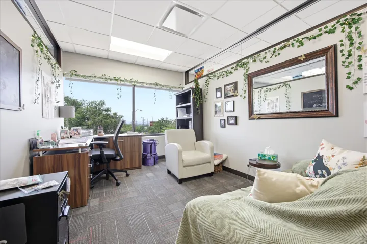 Expansive window offering abundant natural light, wood-finish cabinetry, built-in shelving, suspended ceiling, and carpet tile flooring