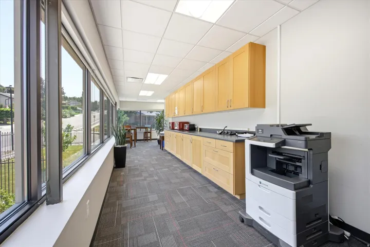 Full-height windows, modular ceiling tiles with recessed lighting, wood-finish cabinetry, and dark countertop surfaces