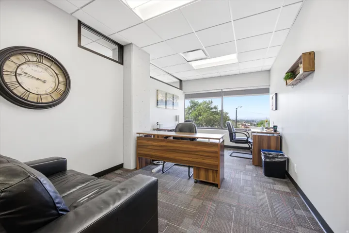 Modular carpet flooring, drop ceiling with integrated lighting, expansive window, wood-finish desk, and a built-in transom window