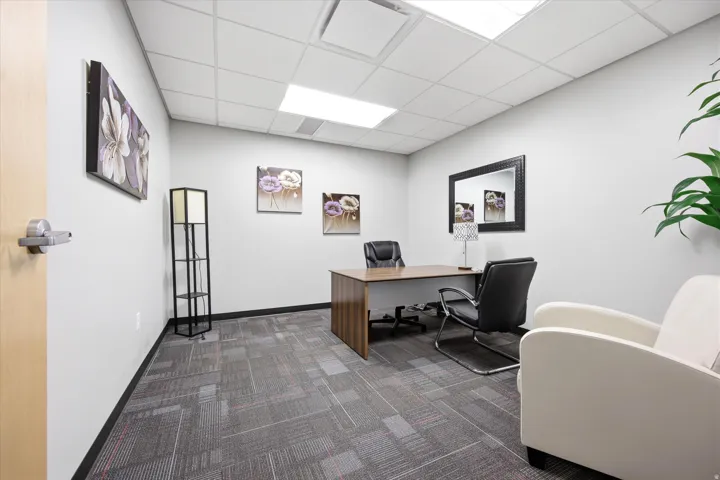 Recessed lighting, drop ceiling, light wood-finish door, light gray walls, and patterned carpet flooring