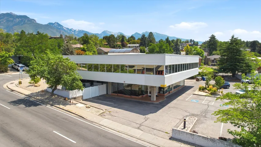 Modern commercial building with expansive window lines, integrated parking, and surrounding mature landscaping