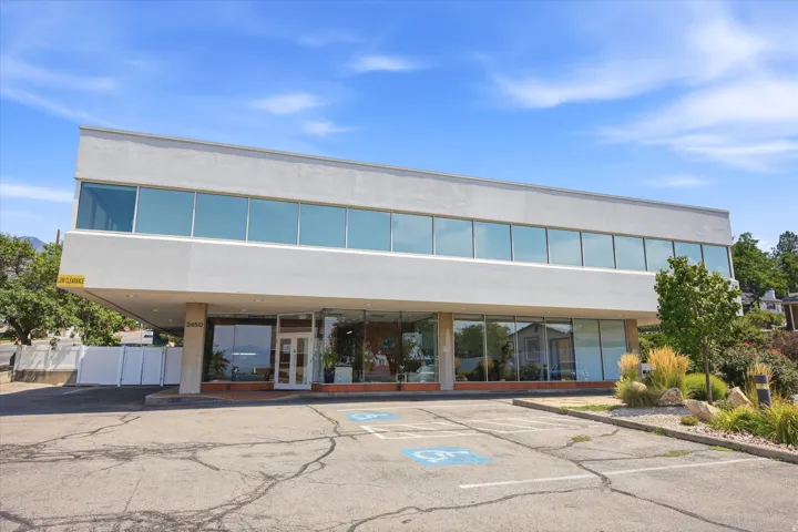 Modern commercial building featuring expansive storefront windows, a contemporary light gray exterior, and a paved parking area
