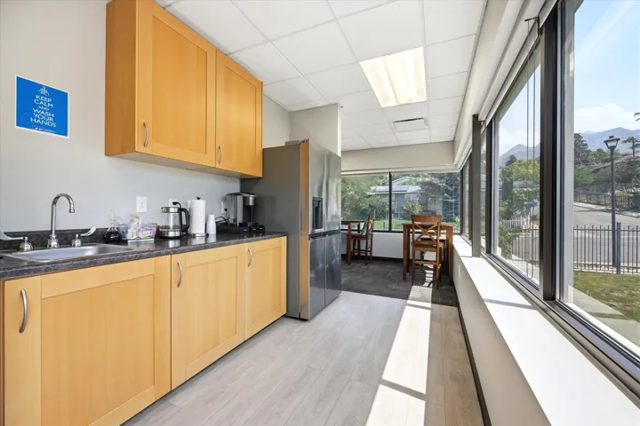 Integrated kitchen with wood-finish cabinetry, stainless steel refrigerator, and a stainless steel sink with a gooseneck faucet