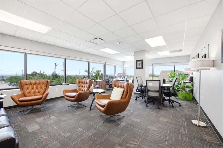 Open-concept office space featuring large windows, patterned carpet flooring, and a drop ceiling with integrated lighting