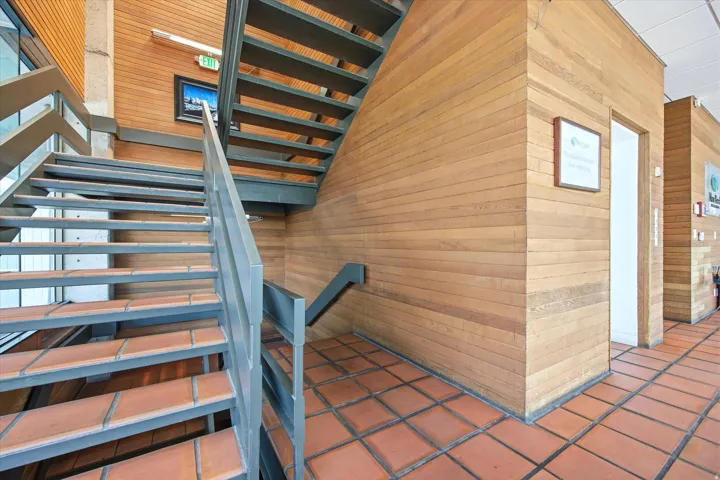 Metal staircase with tiled treads, wood-paneled walls, and terracotta tile flooring