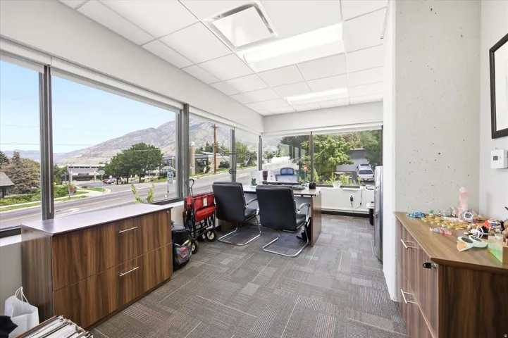 Bright, modern commercial or office space featuring expansive floor-to-ceiling windows with mountain and landscape vistas, wood-finish cabinetry with integrated storage, polished concrete flooring, recessed and skylight ceiling systems, and open floor pla