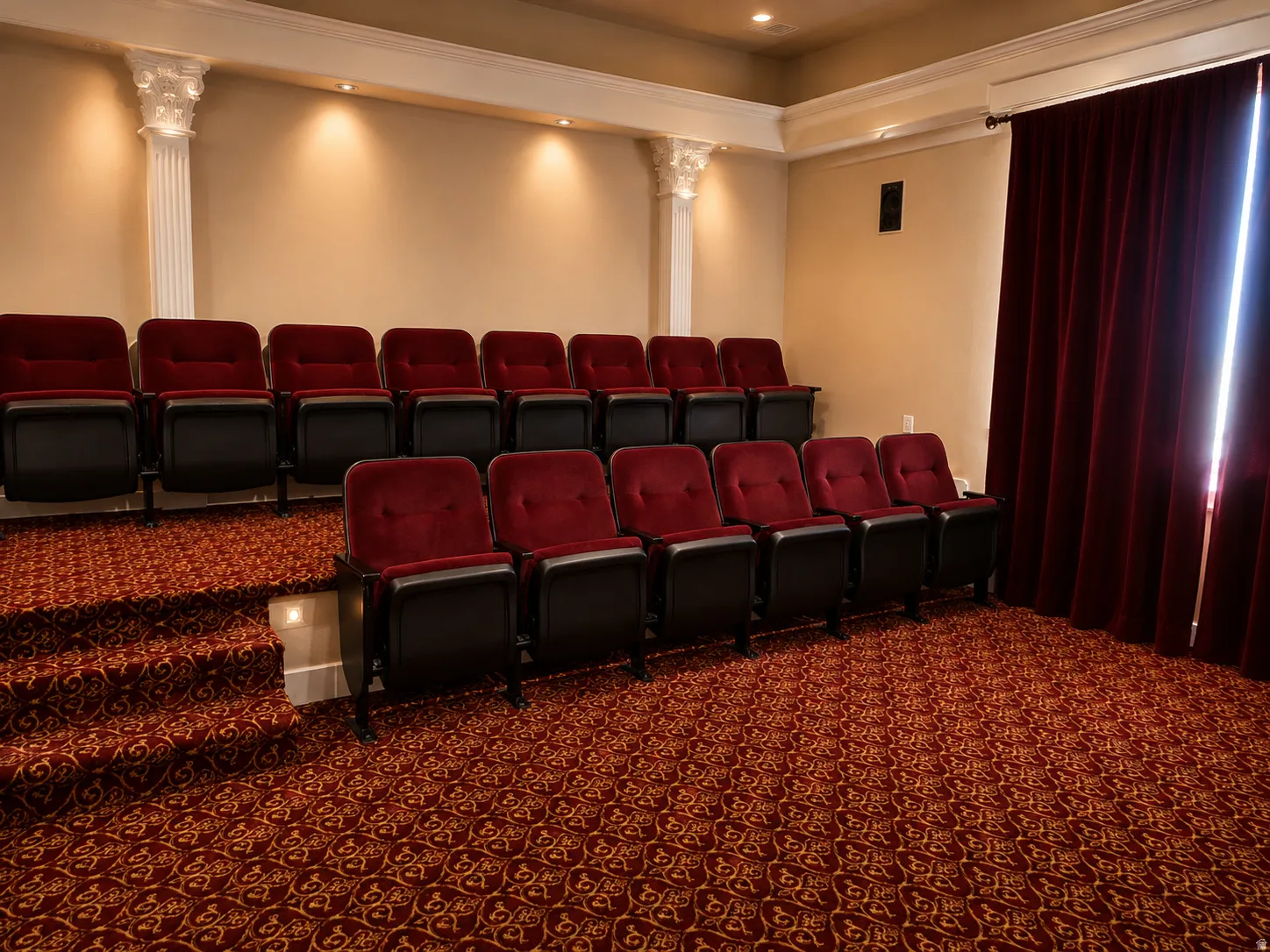 Tiered seating with upholstered chairs, ornate patterned carpet, decorative architectural columns, and recessed lighting
