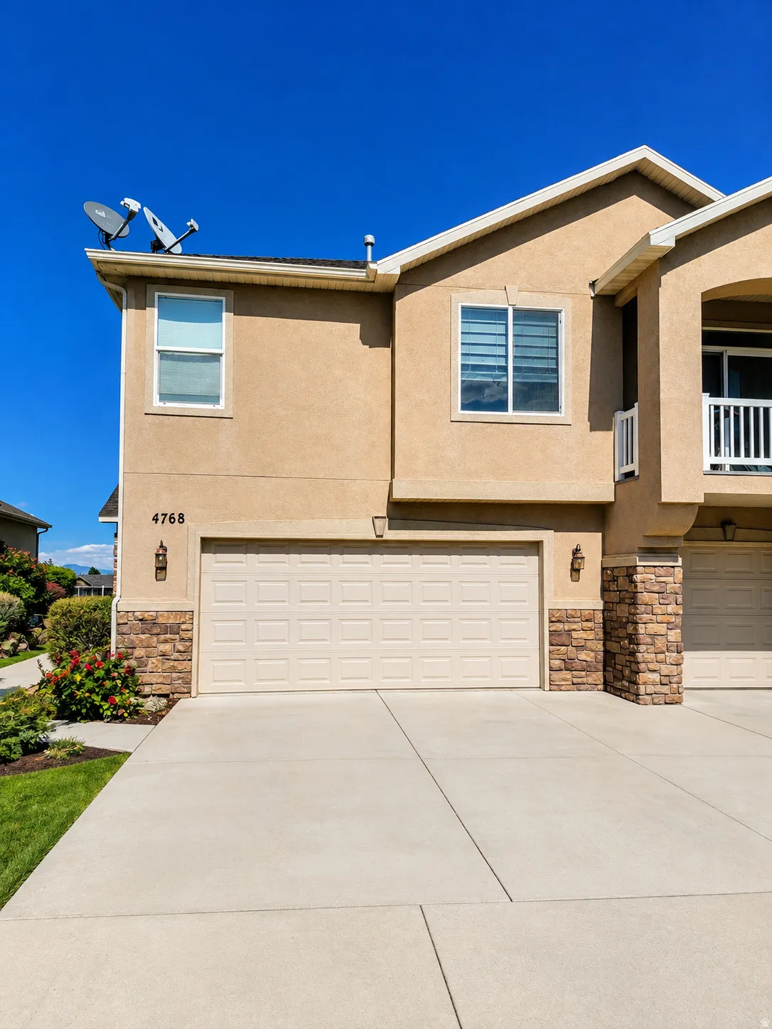 Stucco exterior with stone accents, an attached garage, a concrete driveway, and exterior lighting fixtures
