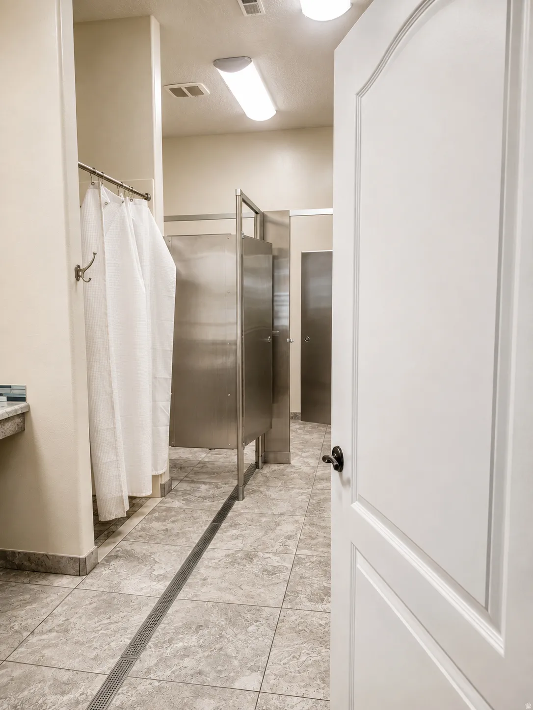 Tiled flooring with linear drain, multiple shower stalls with metal partitions, and a built-in vanity with a tiled backsplash
