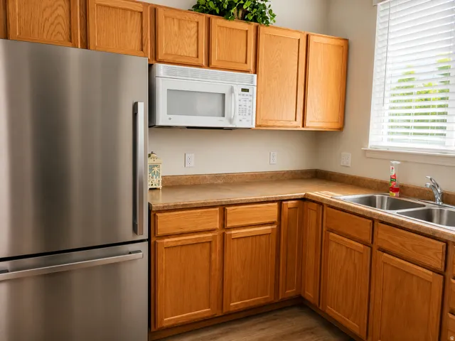 Stainless steel refrigerator, integrated microwave, wood-finish cabinetry, dual basin sink, and composite countertops