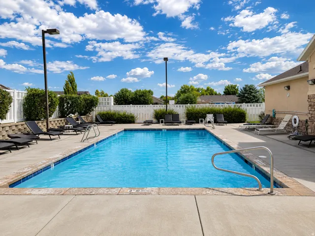 Rectangular swimming pool with concrete decking, surrounding privacy fencing, and exterior building facade